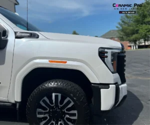 Close-up profile view highlighting the front wheel, fender, headlight, and hood of a white GMC Sierra truck.